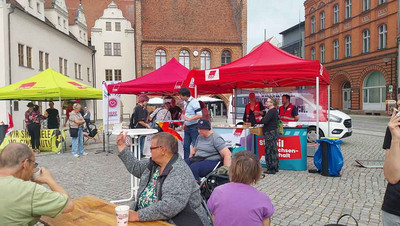 Menschen sitzen an Bänken vor Infoständen.