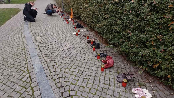 Zwei hockende Menschen fotografieren Schuhpaare auf der Straße.