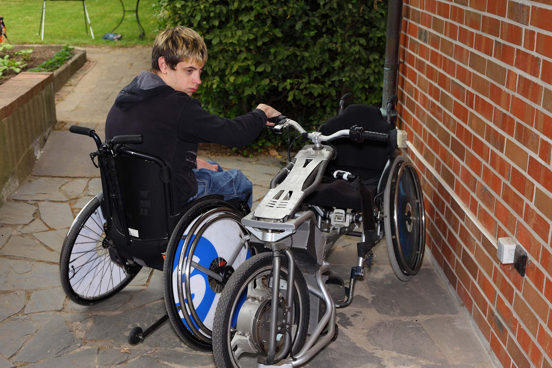 Junger Mann in einem Rollstuhl neben einem Handbike