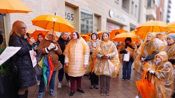 Viele Frauen mit Orangenen Regenschirmen stehen auf der Straße