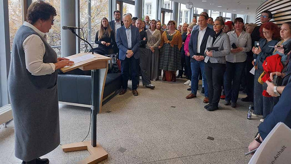 Frau am Stehpult redet vor Menschenmenge.