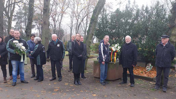 Eine Gruppe Menschen mit Blumen auf dem Friedhof.