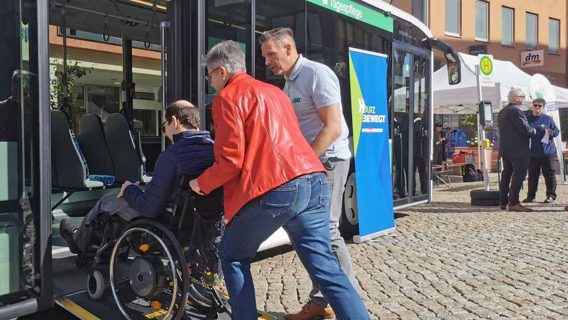 Ein Mann und eine Frau schieben einen Rollstuhlfahrer auf eine Busrampe