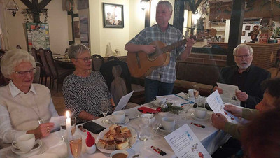 Mann mit Gitarre spielt an einem besetzten Tisch.