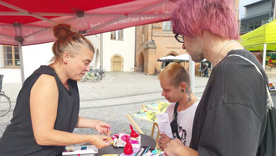 Frau spricht mit zwei Jugendlichen am Infostand.