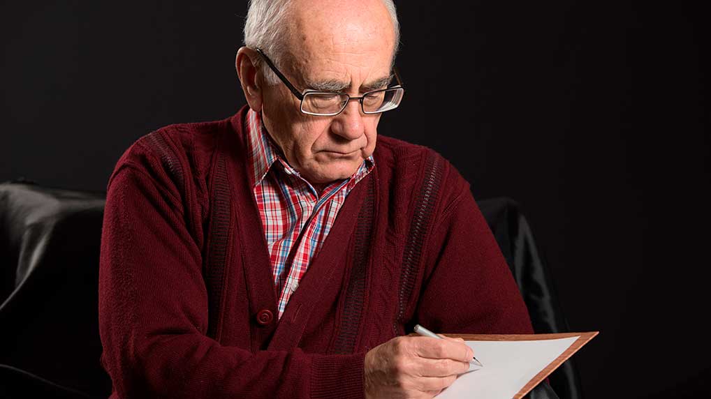 Älterer Mann schreibt auf einem Blatt Papier. 