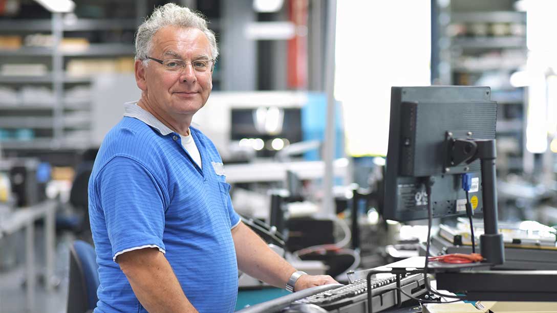 Älterer Mann steht bedient eine Maschine in der Fabrik. 