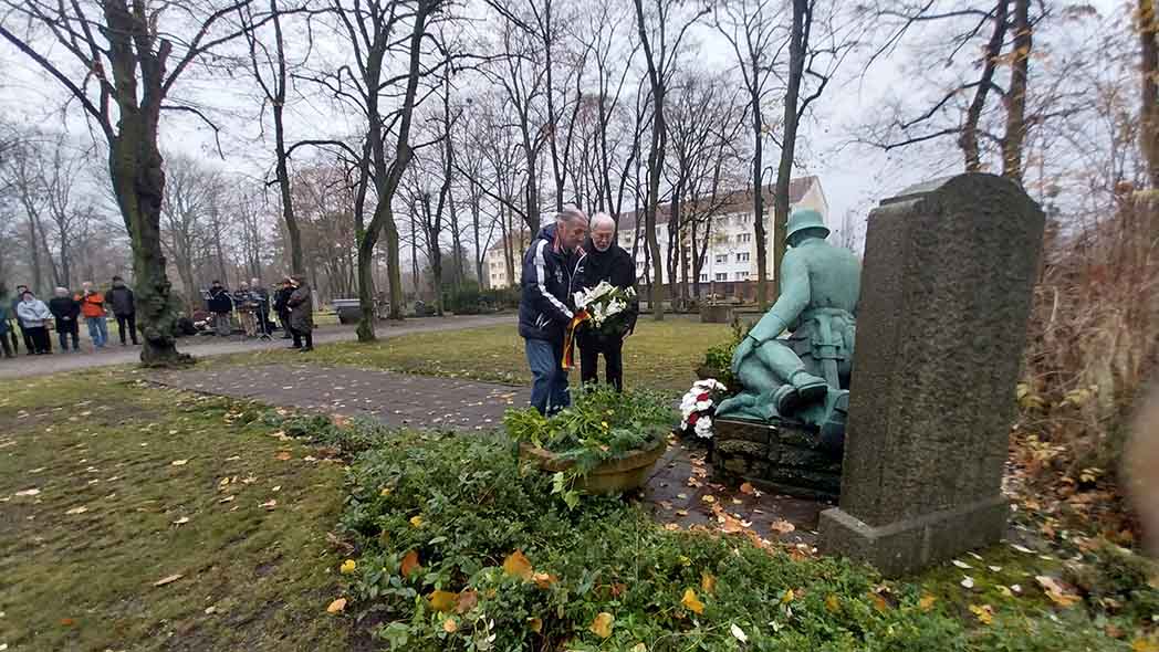 Zwei Männer legen Blumen am Grabmal ab.